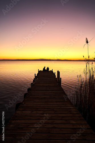 a couple on a pier watching the sunset on a lake                              