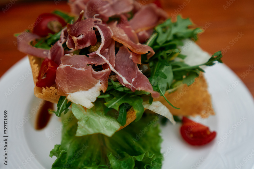 Delicious green salad with jamon and vegetables on a plate served in restaurant