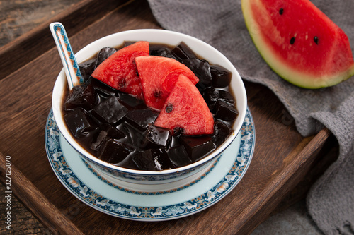 Black Grass Jelly Mesona chinensis, vegetable jelly, black in color, eaten with sugar. Pieces of grass jelly cut in bowl with colorful fruits on top (known as chaokuai, suong sao ) photo