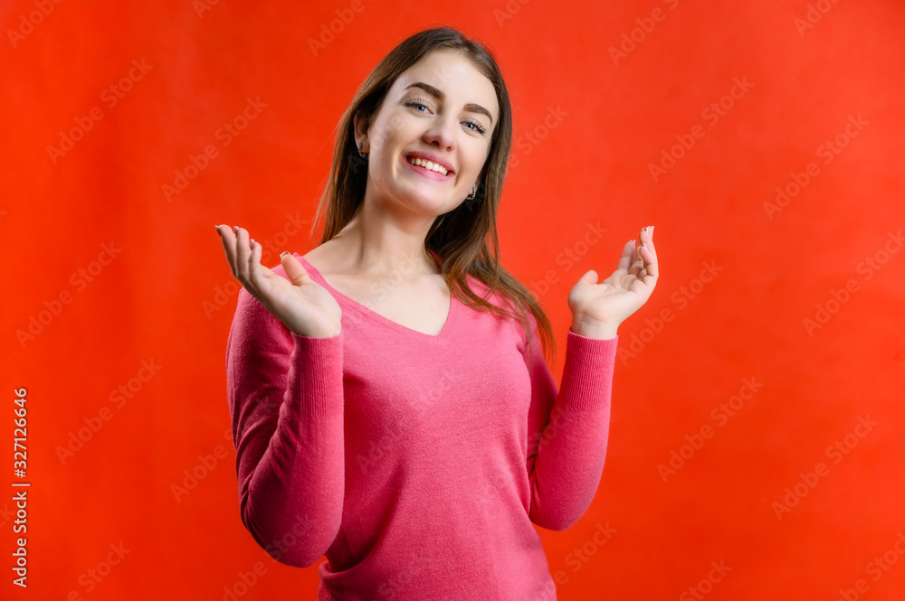 Fototapeta premium Photo on a red background of a pretty smiling woman in a pink sweater showing joy