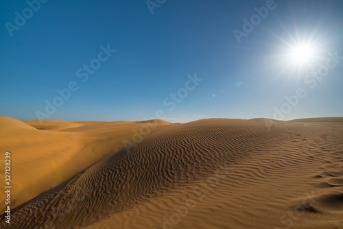 Desert landscape. Beautiful golden sand dunes, blue sky, sun and sun rays. Gran Canaria desert. Maspalomas, South Gran Canaria, Spain