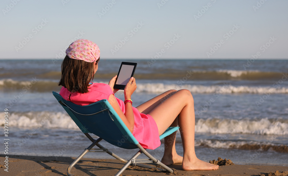 young girl reads an ebook on the beach