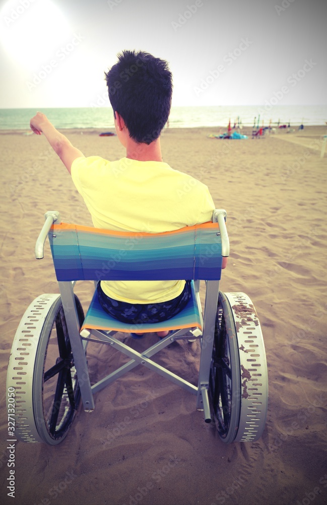young boy on the special wheelchair with big wheels on the beach Stock