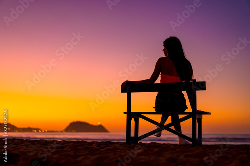 Beautiful silhouette of a brunette looking left in a chair on the beach on a sunset looking at the sea