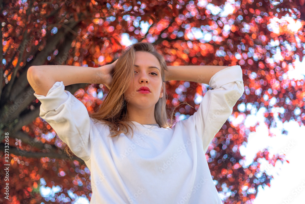 Street Style, a young Caucasian blonde with a white pullover under a red tree in autumn Street Style, a young Caucasian blonde with a white pullover under a red tree in autumn