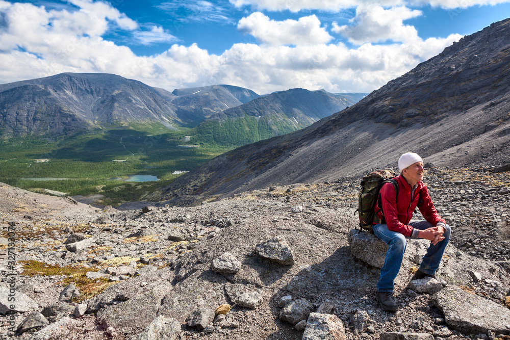 Caucasian senior hiker sitting and resting on stone when climbing to the height of the mountain