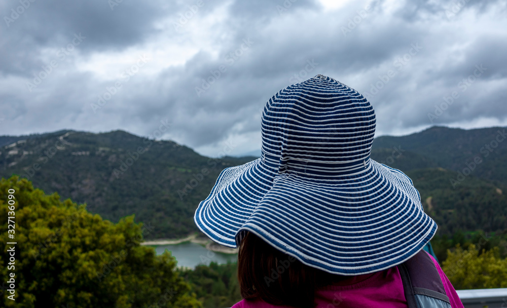 A girl in a wide-brimmed striped hat is watching the mountain landscape.