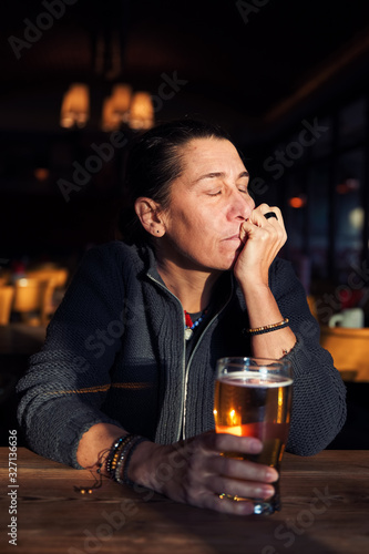 Unhappy, depressed and lonely middle age woman sitting at the bar with a beer glass