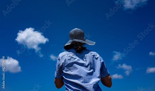 Girl in a wide-brimmed striped hat on a background of blue sky with small clouds