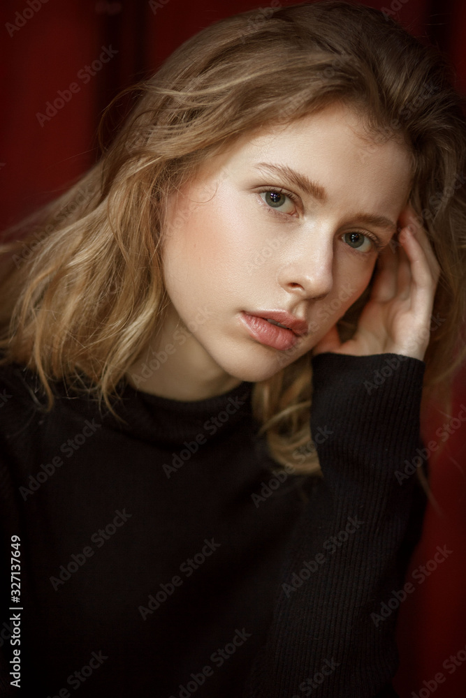 Fototapeta premium portrait of a young beautiful girl with blond hair on a red background with natural light