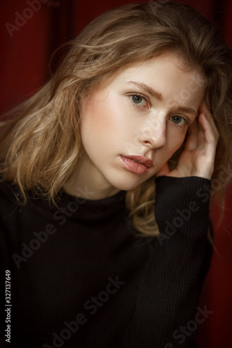  portrait of a young beautiful girl with blond hair on a red background with natural light © Настасья Паршина