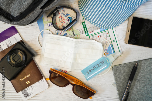 Top view or flat lay of face mask and sanitizer to protect against Coronavirus or COVID-19 and  necessary traveler accessories on white wooden background , COVID 19 virus prevention and travel concept