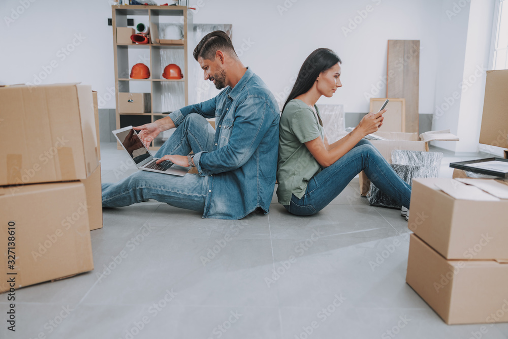 Couple with gadgets sitting backs to each other Couple with gadgets sitting backs to each other