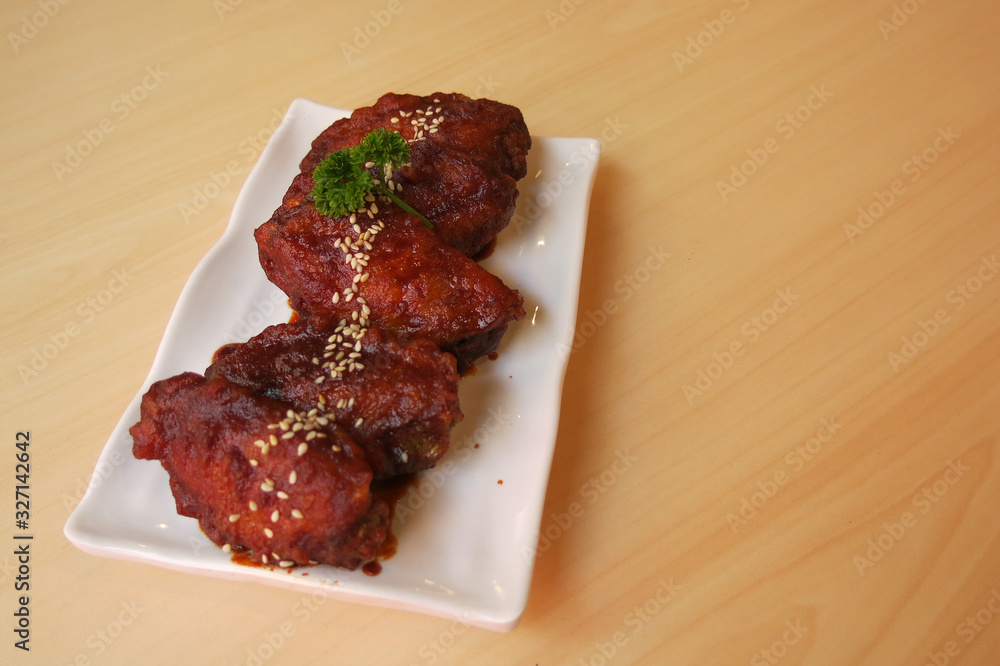 chicken wings with Korea sauce and white sesame in the white plate placing on the brown wooden table chicken wings with Korea sauce and white sesame in the white plate placing on the brown wooden table