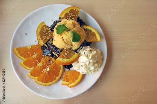  a plate of chocolate toast with some topping which are ice cream, wipe cream, orange and peppermint placing on the brown wooden table
