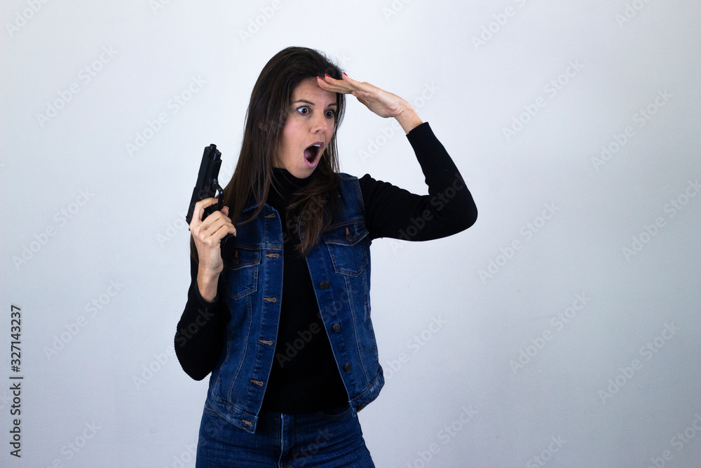 Portrait of attractive caucasian middle age woman with gun being surprised, opening her eyes and mouth with shock, touching her head with hands, isolated on gray background studio shot, black sweater, Portrait of attractive caucasian middle age woman with gun being surprised, opening her eyes and mouth with shock, touching her head with hands, isolated on gray background studio shot, black sweater,