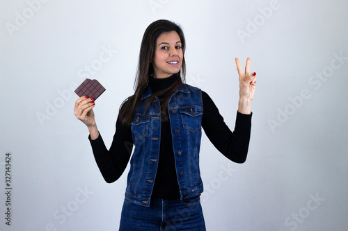 Simbolo de victoriapretty caucasian middle age woman with chocolate making victory or peace sign, isolated on gray background studio shotblack sweater, denim jacket, jeans, dark air. Place for your te photo