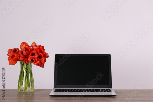 Fresh flower composition  bouquet of darwin hybrid tulips with black and white laptop computer  white wall background. Office romance concept. Copy space  close up  top view  flat lay.