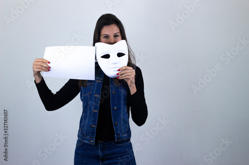 Portrait of happy pretty  middle age womanwhite mask smiling holding a big white placard, sign copy space, isolated on gray background studio shotblack sweater, denim jacket, jeans, dark air. Place fo photo