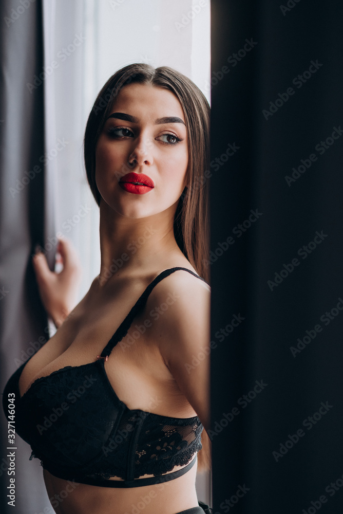 a young girl with dark hair, brown eyes and bright red lips poses in a Studio in black underwear and black trousers a young girl with dark hair, brown eyes and bright red lips poses in a Studio in black underwear and black trousers