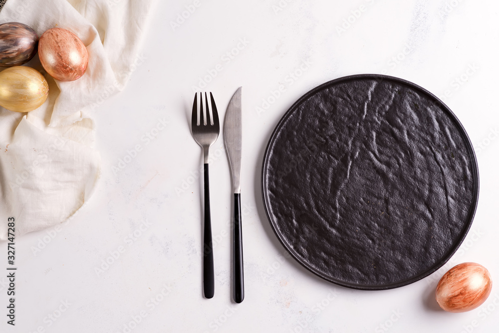 Brown ceramic plate served fork and knife and handcraft painted Easter eggs on a light grey marble background. Brown ceramic plate served fork and knife and handcraft painted Easter eggs on a light grey marble background.