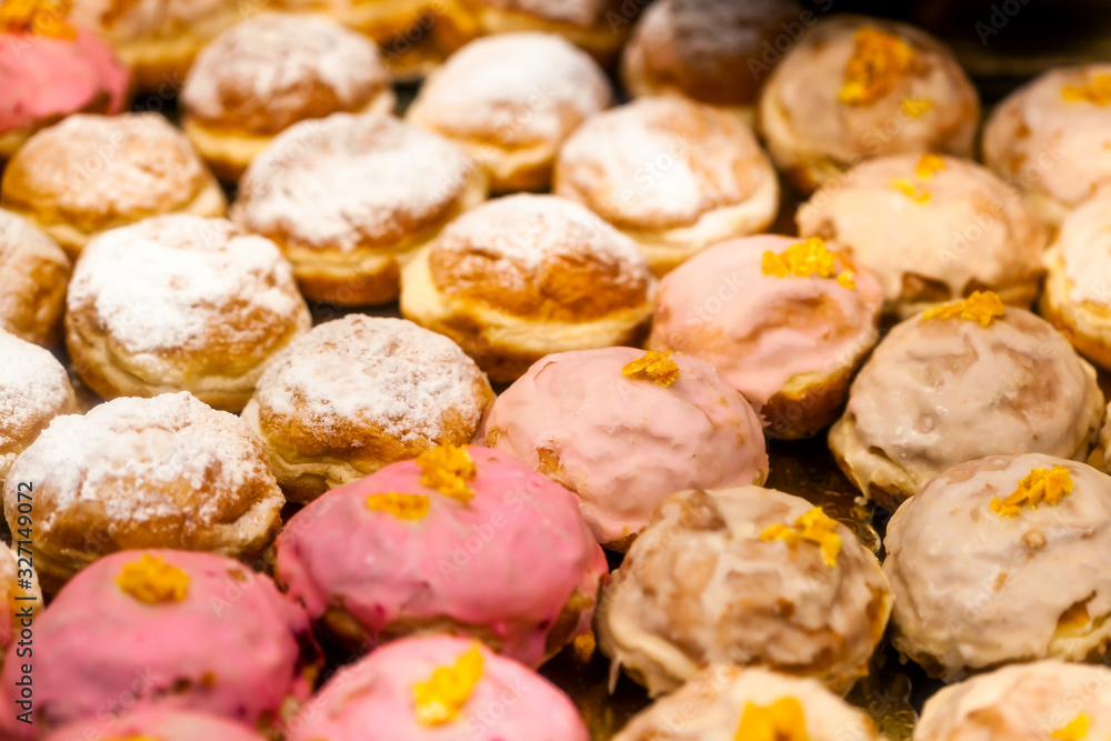 Lots of sweet tasty donuts without a hole, warm background texture pattern. Group of delicious traditional european doughnuts at the bakery fresh from the oven Pink and white, powdered sugar, frosting