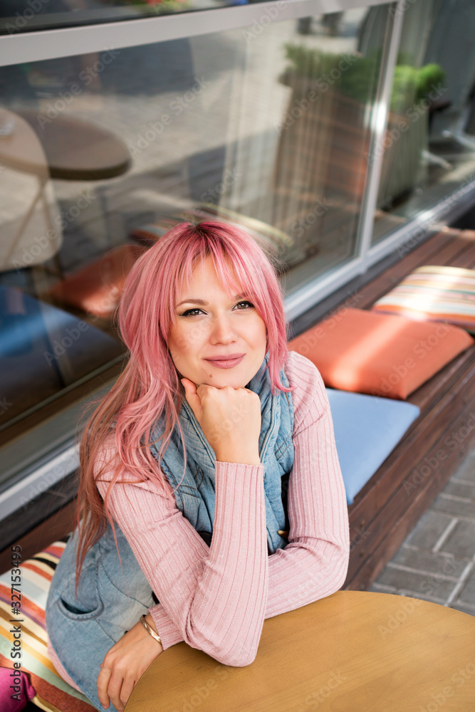 Adorable young woman with long pink hair posing on the summer terrace of the cafe. Last warm days. Sun enjoyment. Carefree girl. Good mood Adorable young woman with long pink hair posing on the summer terrace of the cafe. Last warm days. Sun enjoyment. Carefree girl. Good mood