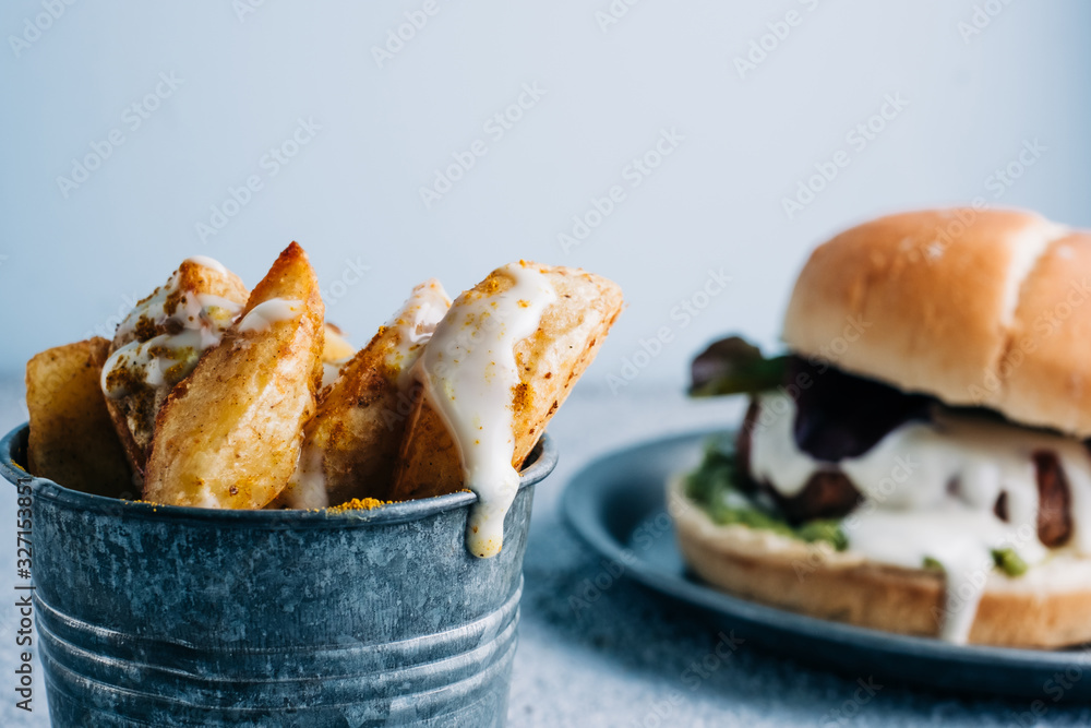 French fries with spices in metal bowl with a burger in background. selective focus French fries with spices in metal bowl with a burger in background. selective focus