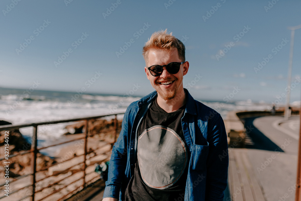 Smiling happy european man with blond hair enjoying his trip and walking near the ocean in sunny day