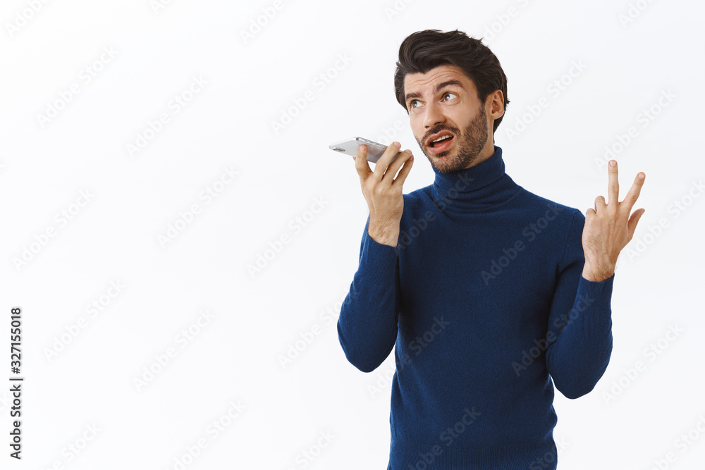 Busy stylish male entrepreneur with bristle, wear blue high neck sweater, record voice message as holding smartphone near mouth, gesturing, complaining about boyfriend, white background Busy stylish male entrepreneur with bristle, wear blue high neck sweater, record voice message as holding smartphone near mouth, gesturing, complaining about boyfriend, white background