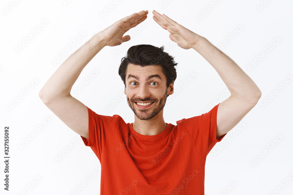 Waist-up portrait handsome young man with bristle, wear red t-shirt raising hands above head as making house roof, smiling joyfully, cant wait celebrate holidays in family circle, white background Waist-up portrait handsome young man with bristle, wear red t-shirt raising hands above head as making house roof, smiling joyfully, cant wait celebrate holidays in family circle, white background