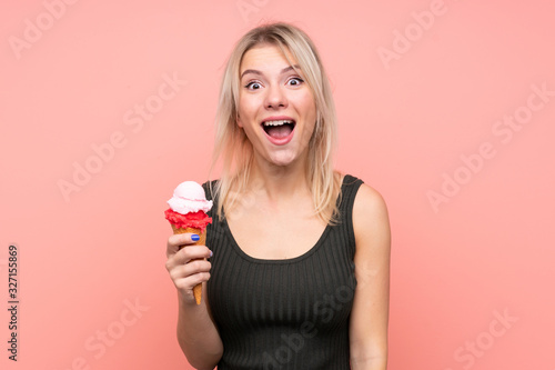 Young blonde woman with a cornet ice cream over isolated pink background with surprise and shocked facial expression