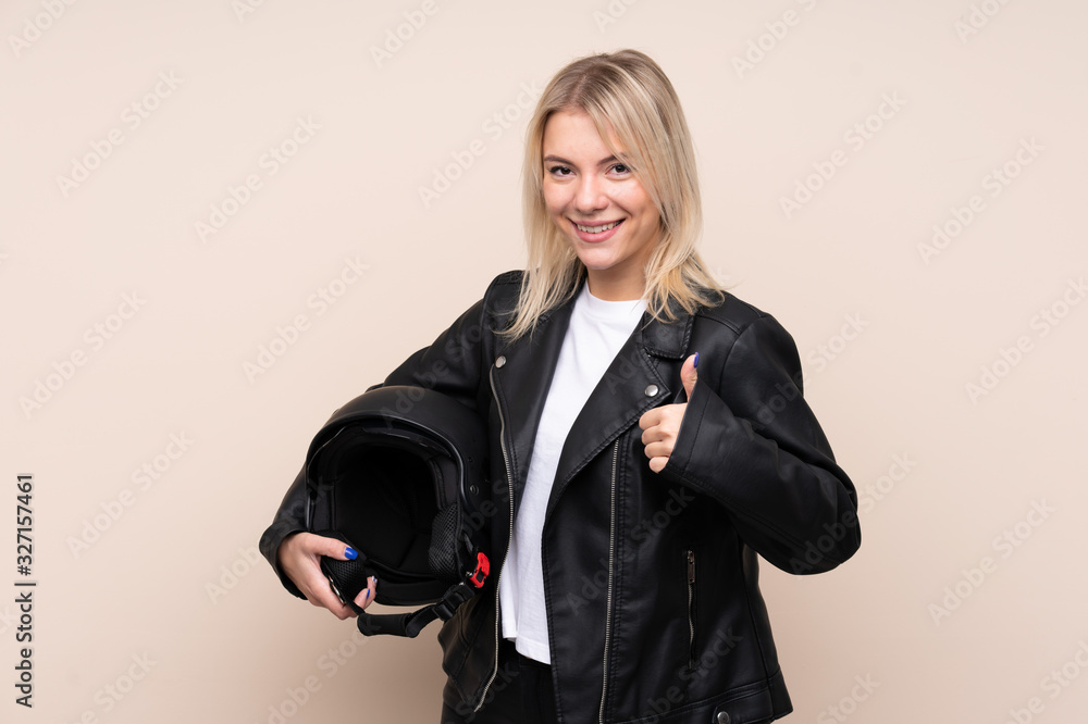 Young blonde woman with a motorcycle helmet over isolated background with thumbs up because something good has happened Young blonde woman with a motorcycle helmet over isolated background with thumbs up because something good has happened
