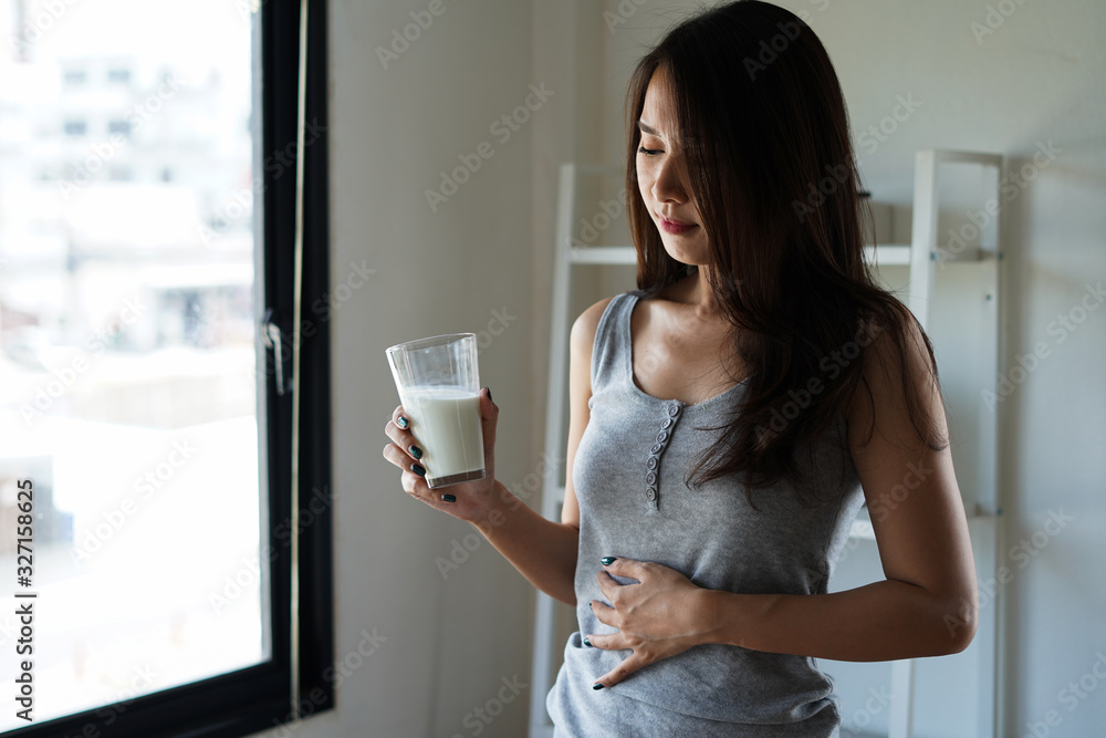 Beautiful asian woman with stomach ache and pain holding a glass of