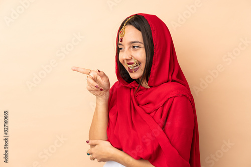 Young Indian woman isolated on beige background pointing finger to the side and presenting a product