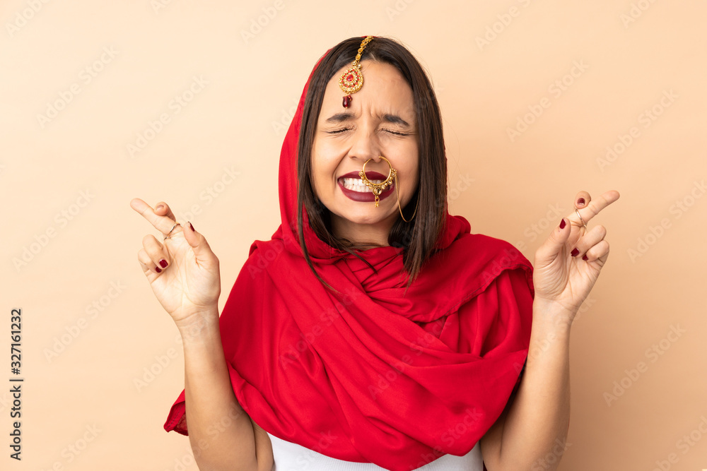 Young Indian woman isolated on beige background with fingers crossing and wishing the best Young Indian woman isolated on beige background with fingers crossing and wishing the best