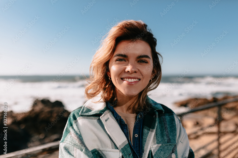 Outside close up portrait of happy woman with flying hair walking against ocean waves Outside close up portrait of happy woman with flying hair walking against ocean waves