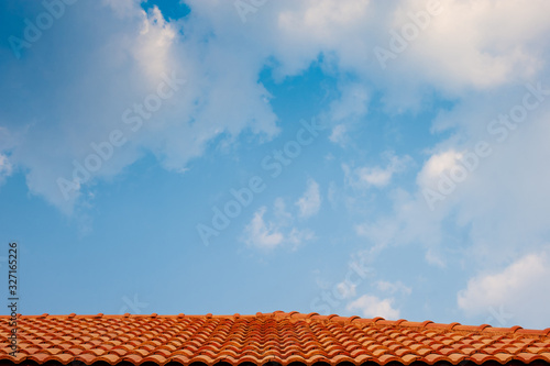 Bright light blue sky with many white and grey chunks of clouds floating background  with red brown concrete wavy corrugated roof as the lower border