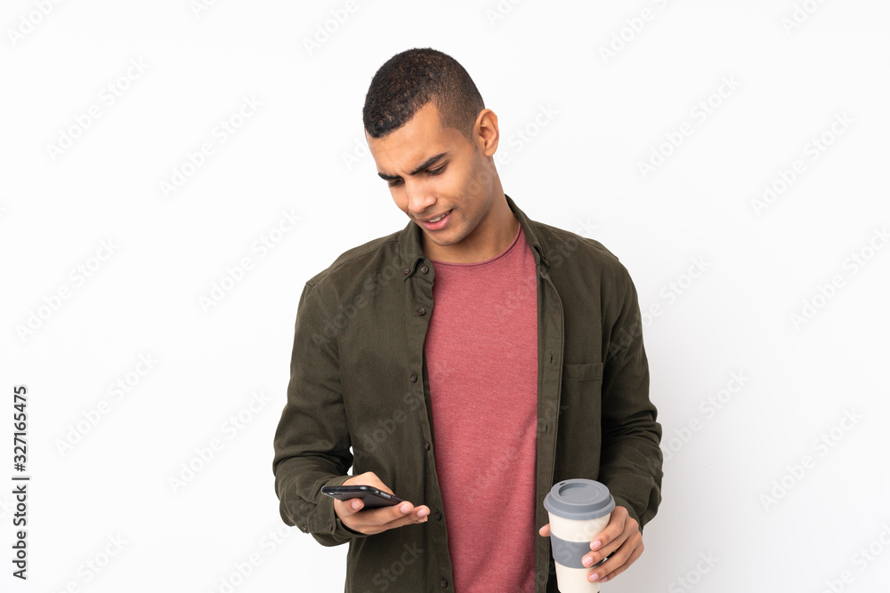 Young African American man over isolated white background holding coffee to take away and a mobile Young African American man over isolated white background holding coffee to take away and a mobile
