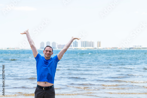 Young happy man with arms up on beach bay with Pensacola cityscape skyline in background in Navarre, Florida Panhandle near Gulf of Mexico