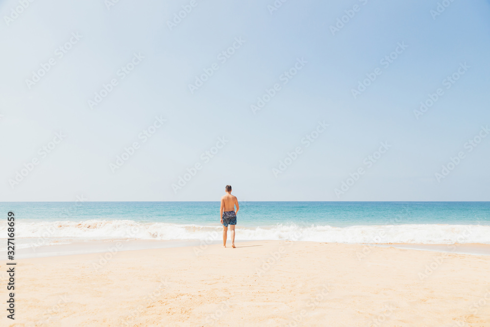Teenage boy, walking into the water, at the ocean sandy beach. Travel and vacation concept.