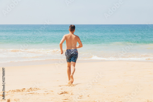 Teenage boy, running into the water, at the ocean sandy beach. Travel and vacation concept.