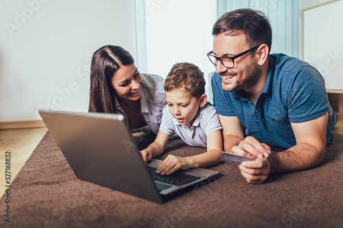 Beautiful parents and their son are doing shopping online using laptop and smiling at home.
