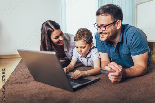 Beautiful parents and their son are doing shopping online using laptop and smiling at home. © Mediteraneo