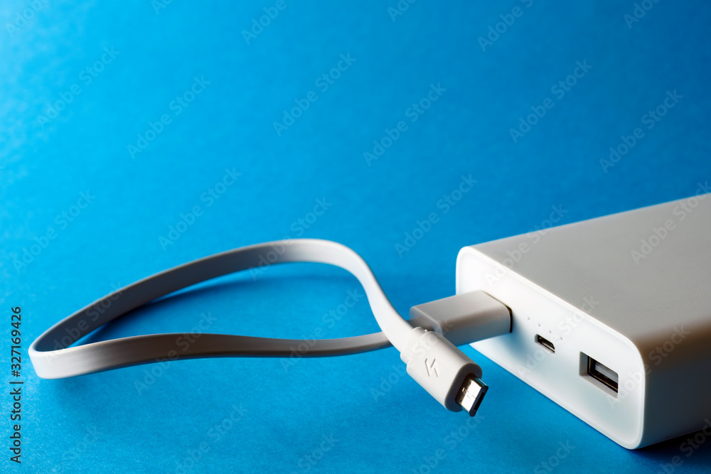 White power bank with micro usb cable in port on blue background. Selective focus, copy space. White power bank with micro usb cable in port on blue background. Selective focus, copy space.