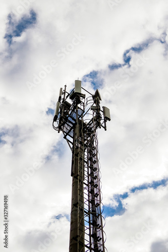 Cellular communications tower on cloudy sky background in daytime.