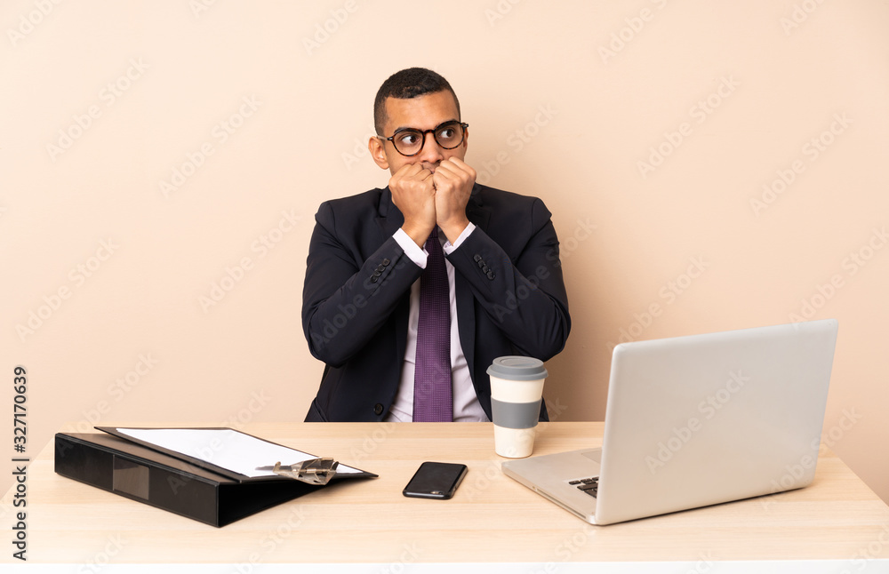Young business man in his office with a laptop and other documents nervous and scared putting hands to mouth Young business man in his office with a laptop and other documents nervous and scared putting hands to mouth