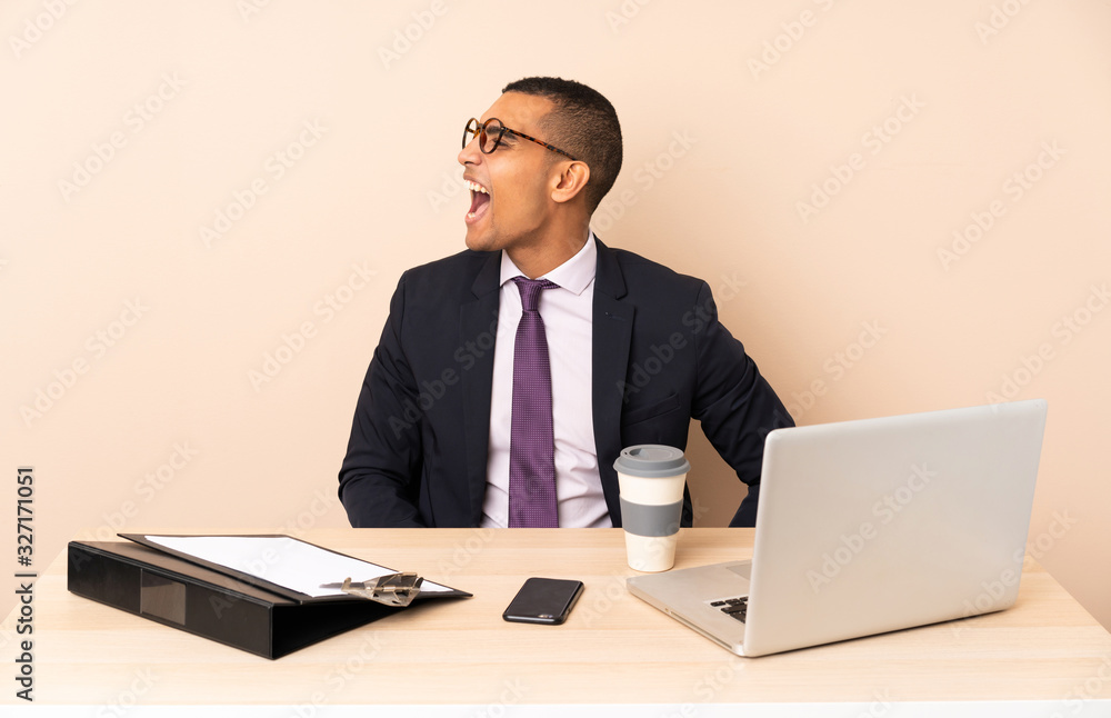 Young business man in his office with a laptop and other documents laughing in lateral position Young business man in his office with a laptop and other documents laughing in lateral position