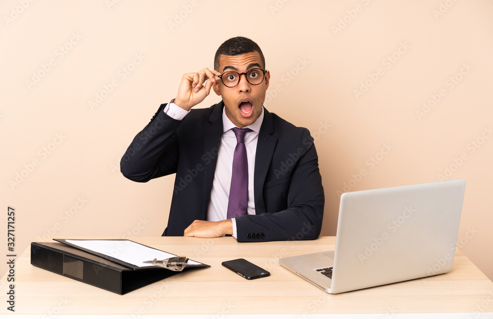 Young business man in his office with a laptop and other documents with glasses and surprised Young business man in his office with a laptop and other documents with glasses and surprised
