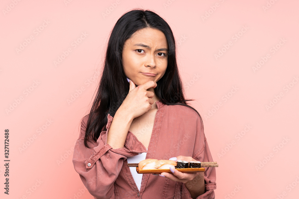 Teenager Asian girl eating sushi isolated on pink background laughing Teenager Asian girl eating sushi isolated on pink background laughing